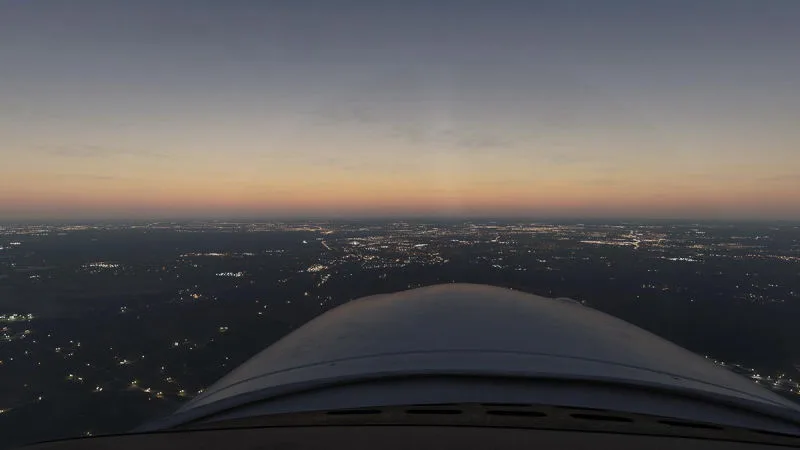 Cockpit nose view over a sprawling city at twilight, REX Atmos CORE lighting in Microsoft Flight Simulator 2024