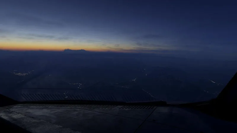 Dusk flight over mountains with a glowing orange horizon and distant city lights, REX Atmos CORE atmospherics in Microsoft Flight Simulator 2024